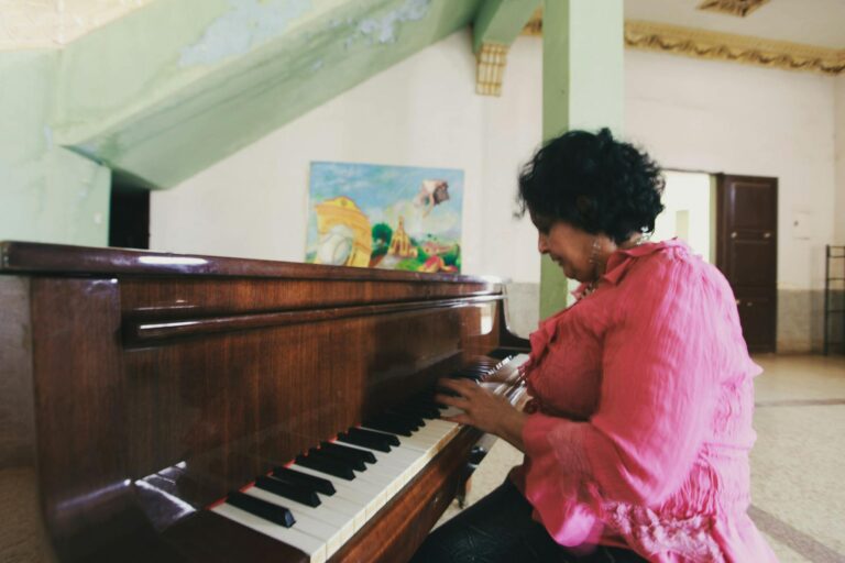A woman in a pink blouse plays piano indoors, focusing on her musical talent.