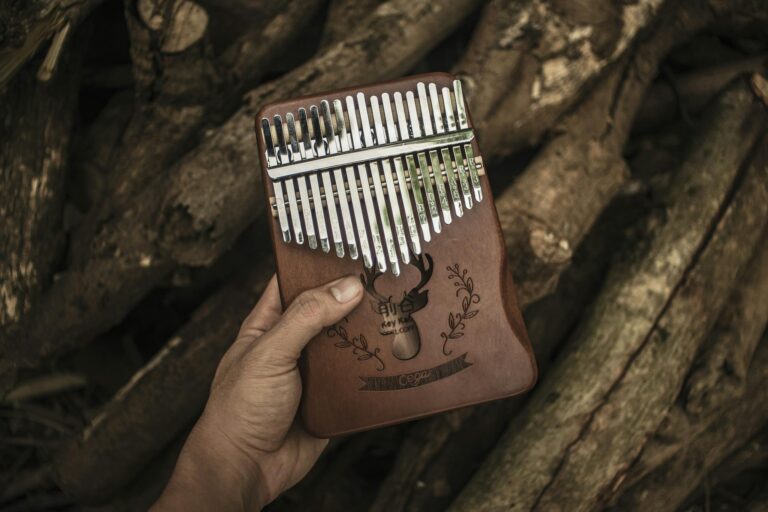 Hand holding a wooden kalimba in front of logs, showcasing the intricate musical instrument with natural background.